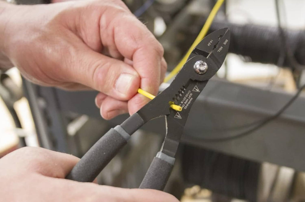 Hand using black multi-function wire stripper pliers to grip a yellow wire