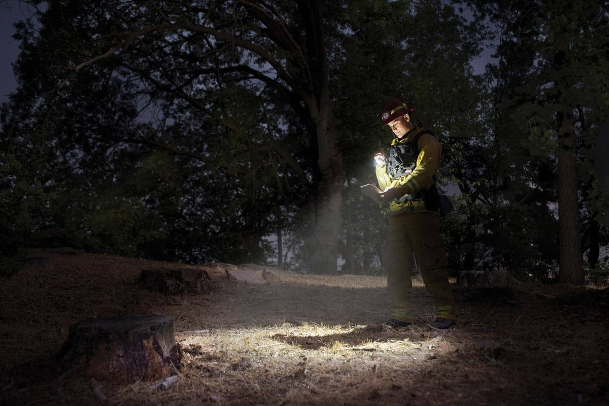 Silver flashlight held in hand, narrow beam illuminating ground at night