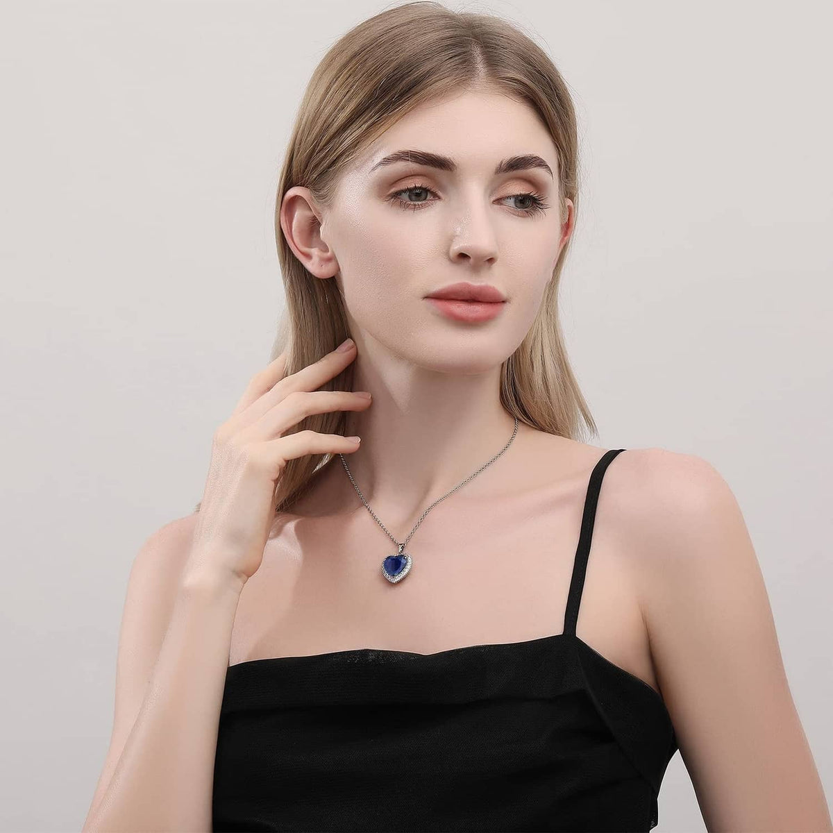 Heart pendant necklace with blue stone on silver chain worn with black top
