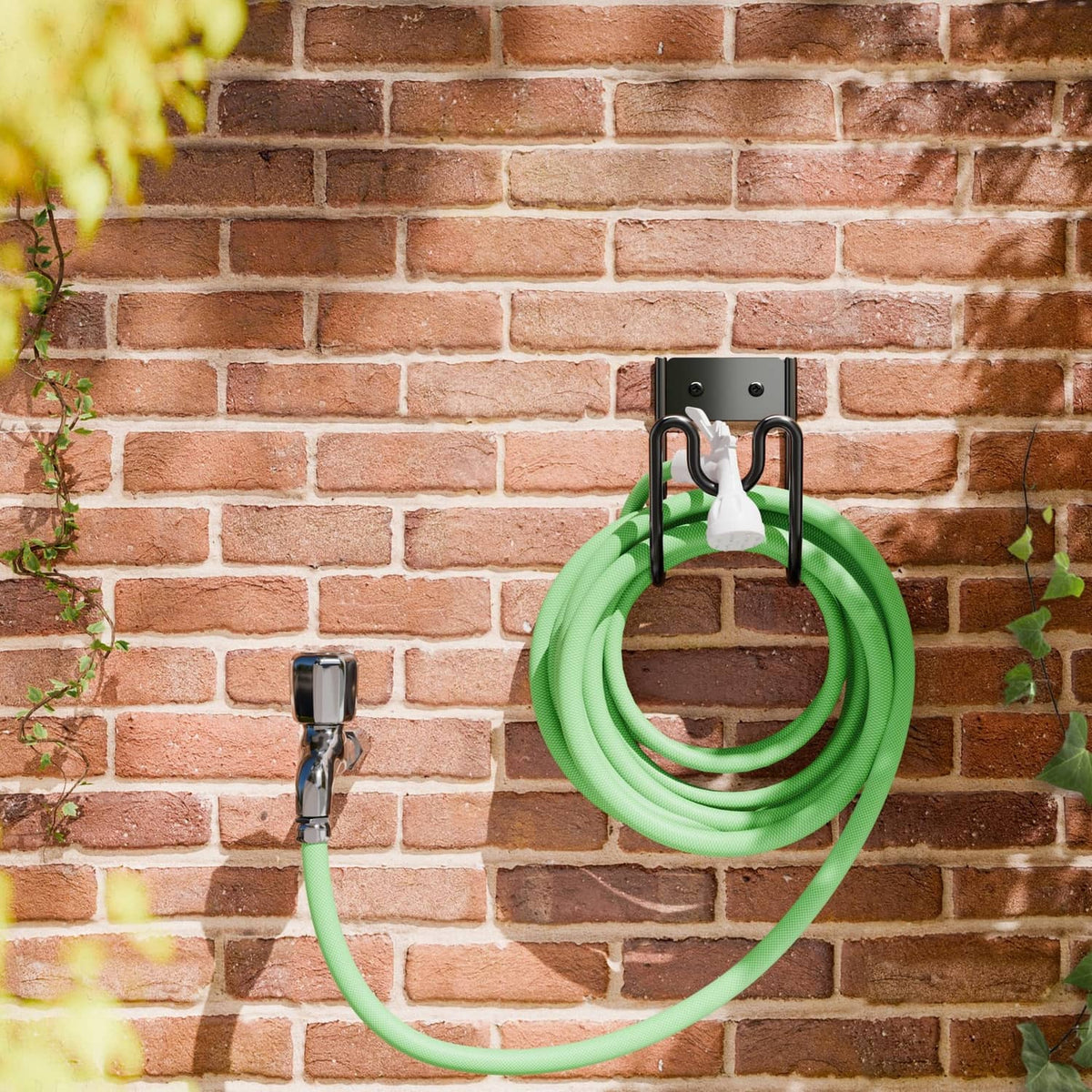 Black metal wall hose holder with two hooks holding green hose on a brick wall