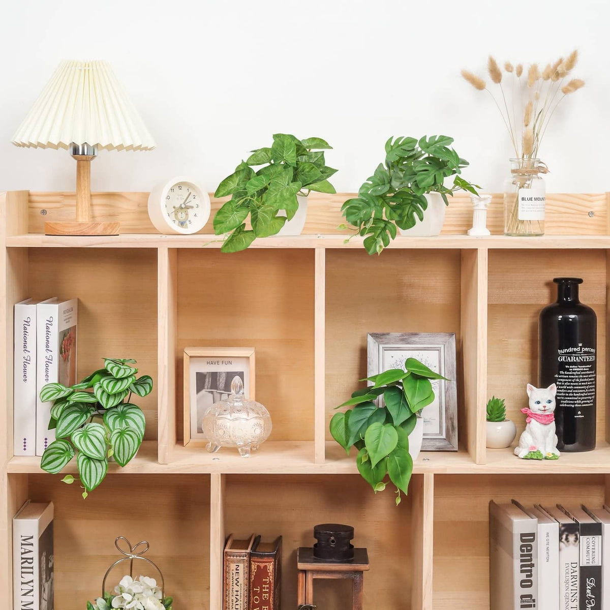 Green leafy artificial plants with vines in white pots on open wooden shelves