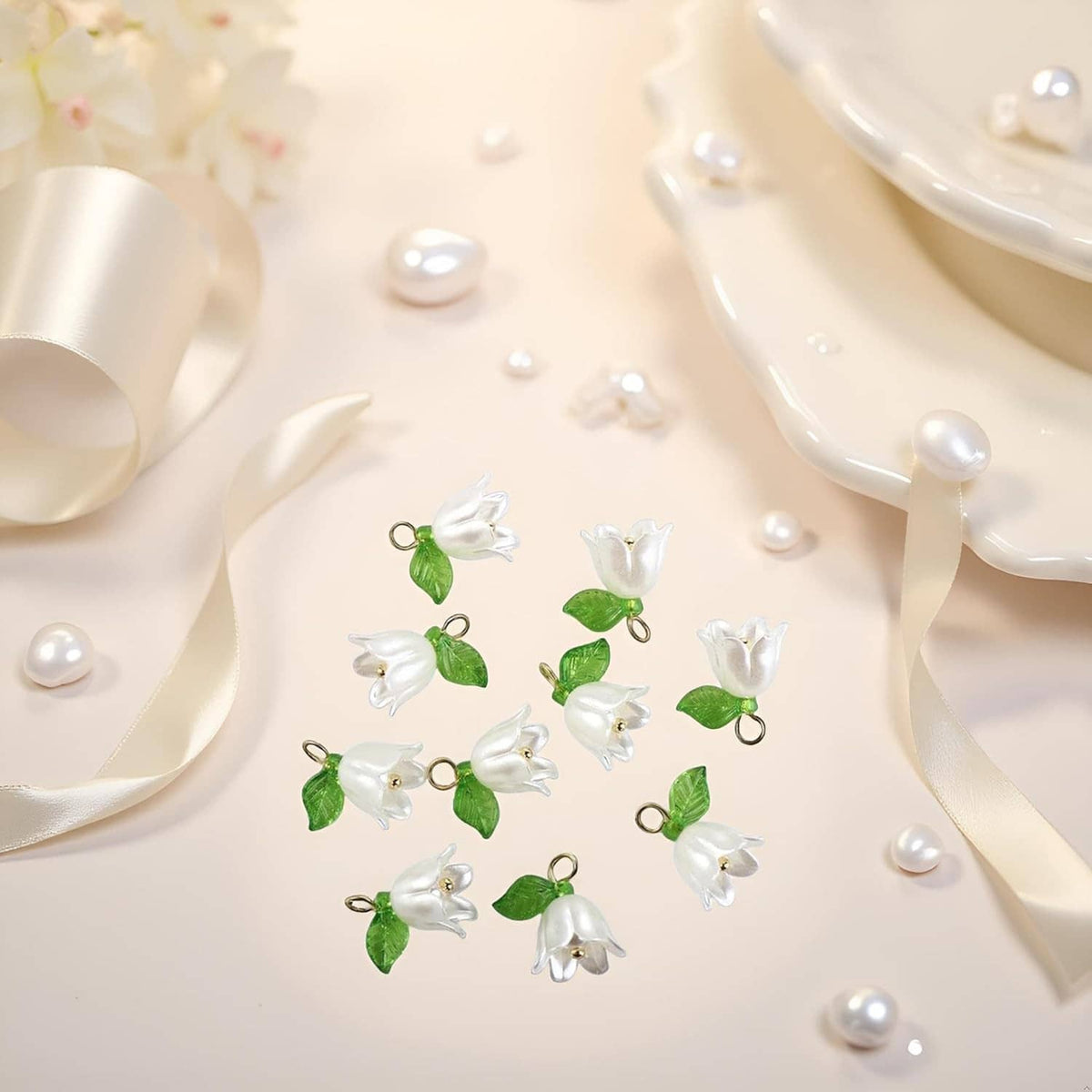 White bell orchid beads with green leaves and gold loop rings, laid out for display