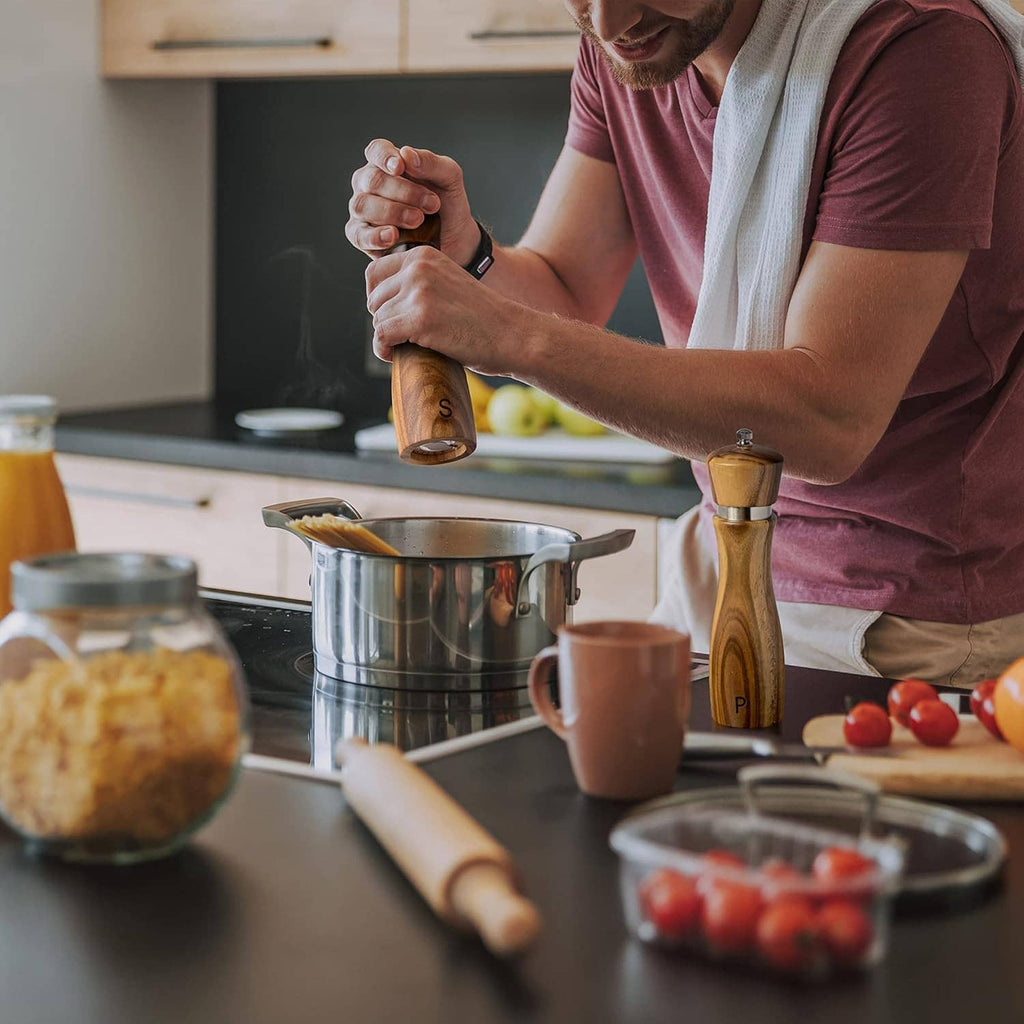 Person using wooden salt and pepper mills at a kitchen counter, holding one by the top