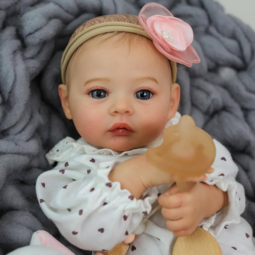 Realistic 18-inch reborn baby girl doll reaching forward, wearing white heart onesie and headband.