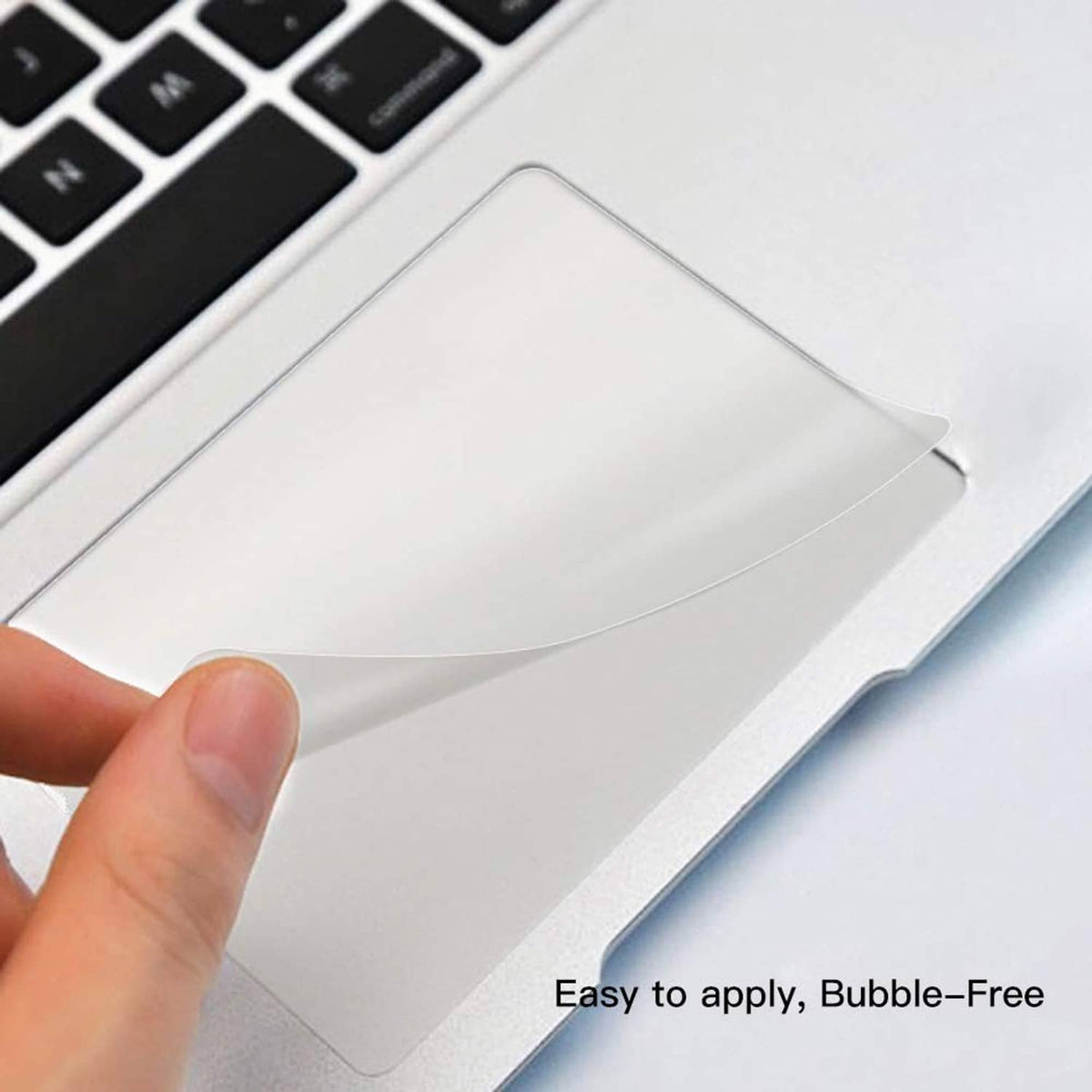 Clear trackpad protector film on a MacBook trackpad, hand applying the flexible sheet.