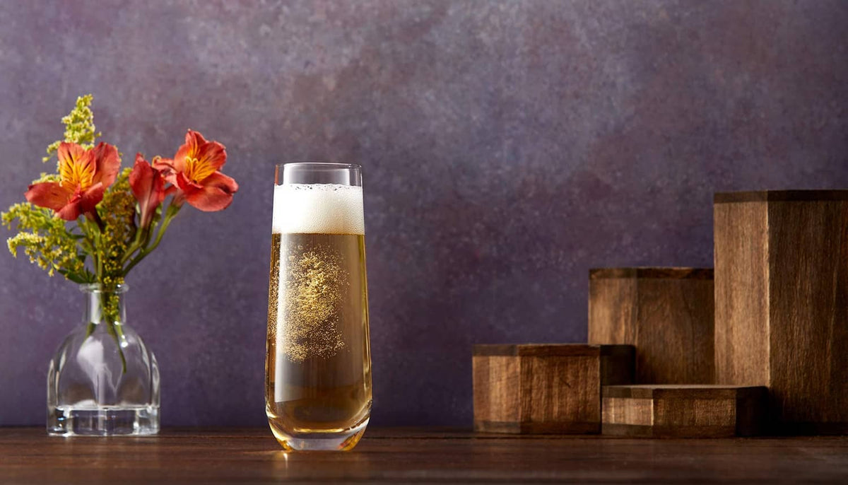 Stemless champagne flute with golden sparkling drink, with flowers in a vase