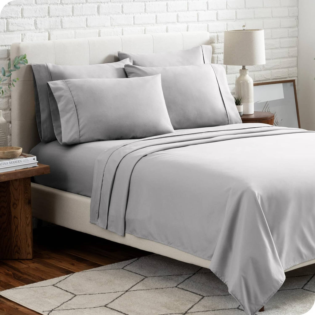 Light grey microfiber bed linen set with two pillows and neatly draped flat/fitted sheets