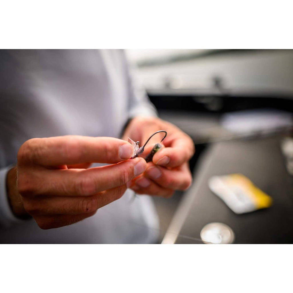 Hands holding small fishing hook with dark lure body and metal ring