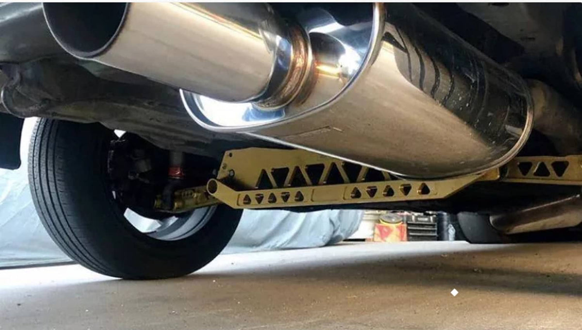 Close-up of silver rear subframe brace tie bar under car, near exhaust pipe