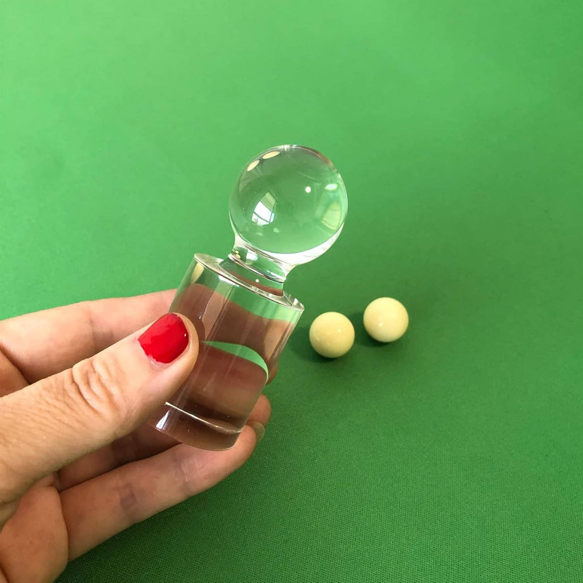 Hand holding clear acrylic roulette marker with round ball top; two pale yellow balls