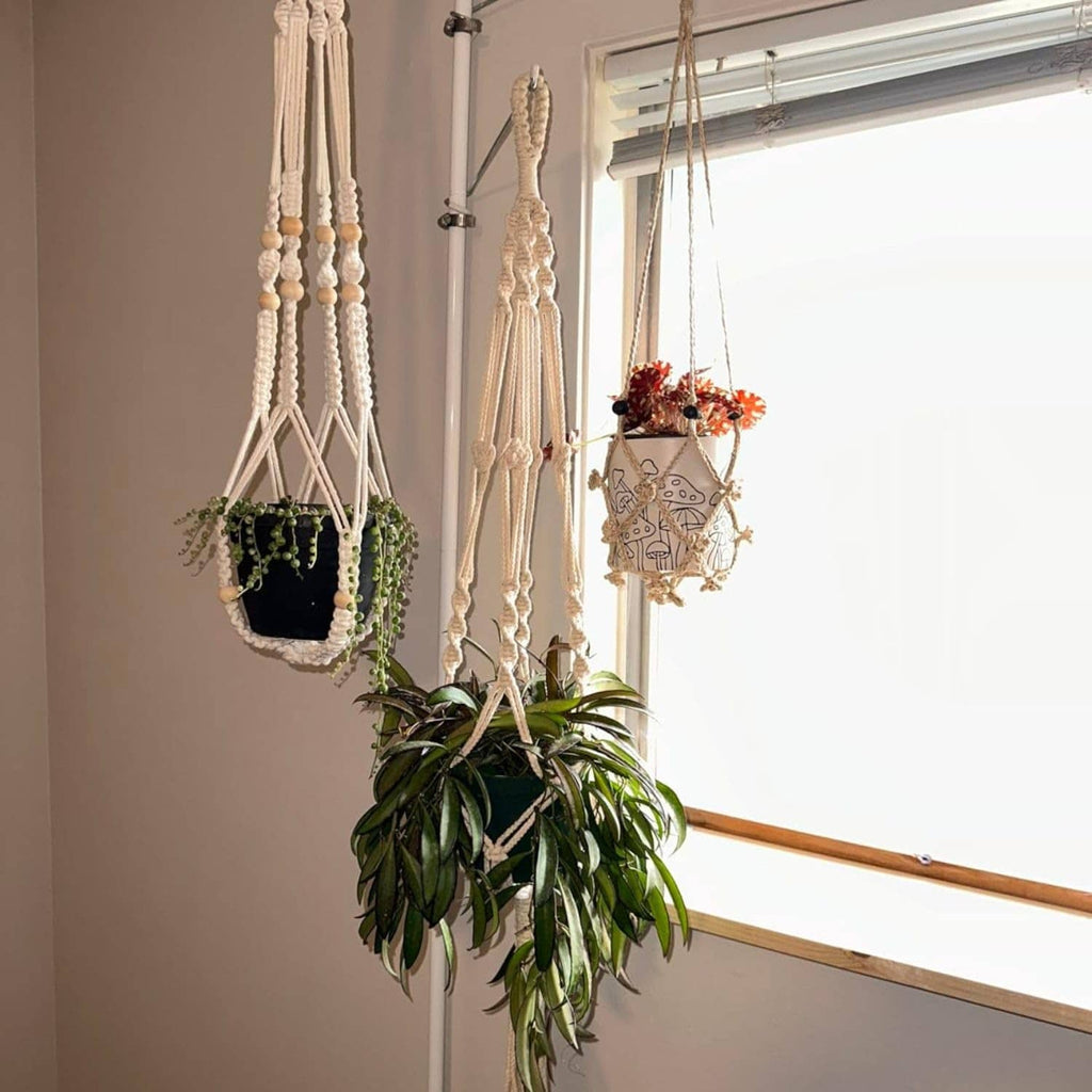 Spring tension rod plant hanger with three adjustable arms holding pots indoors