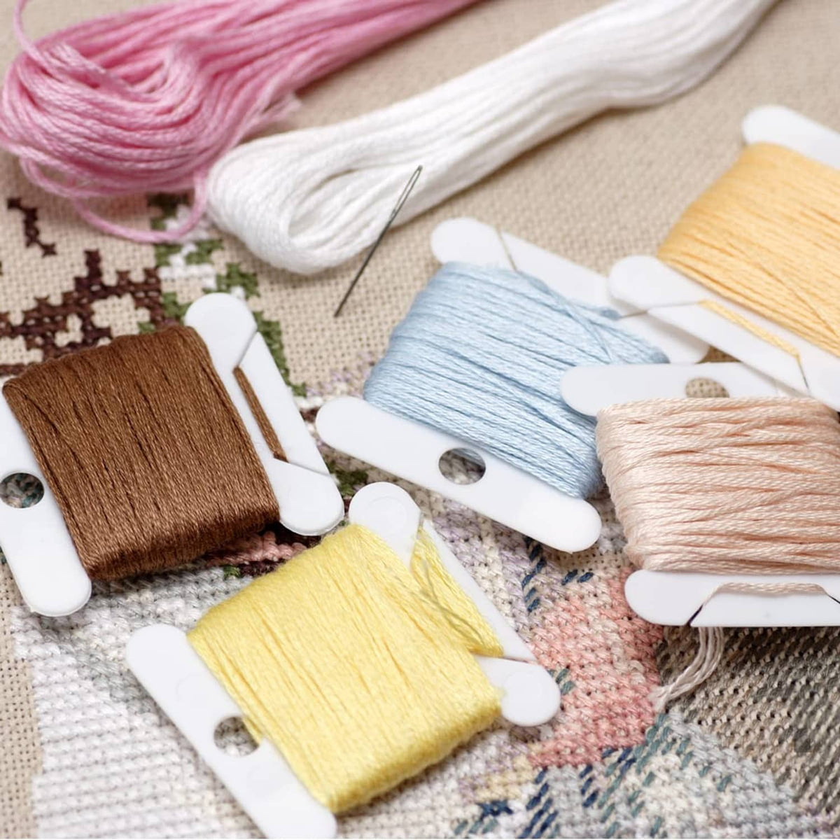 Embroidery floss clips holding light pink, white, blue, and tan thread spools
