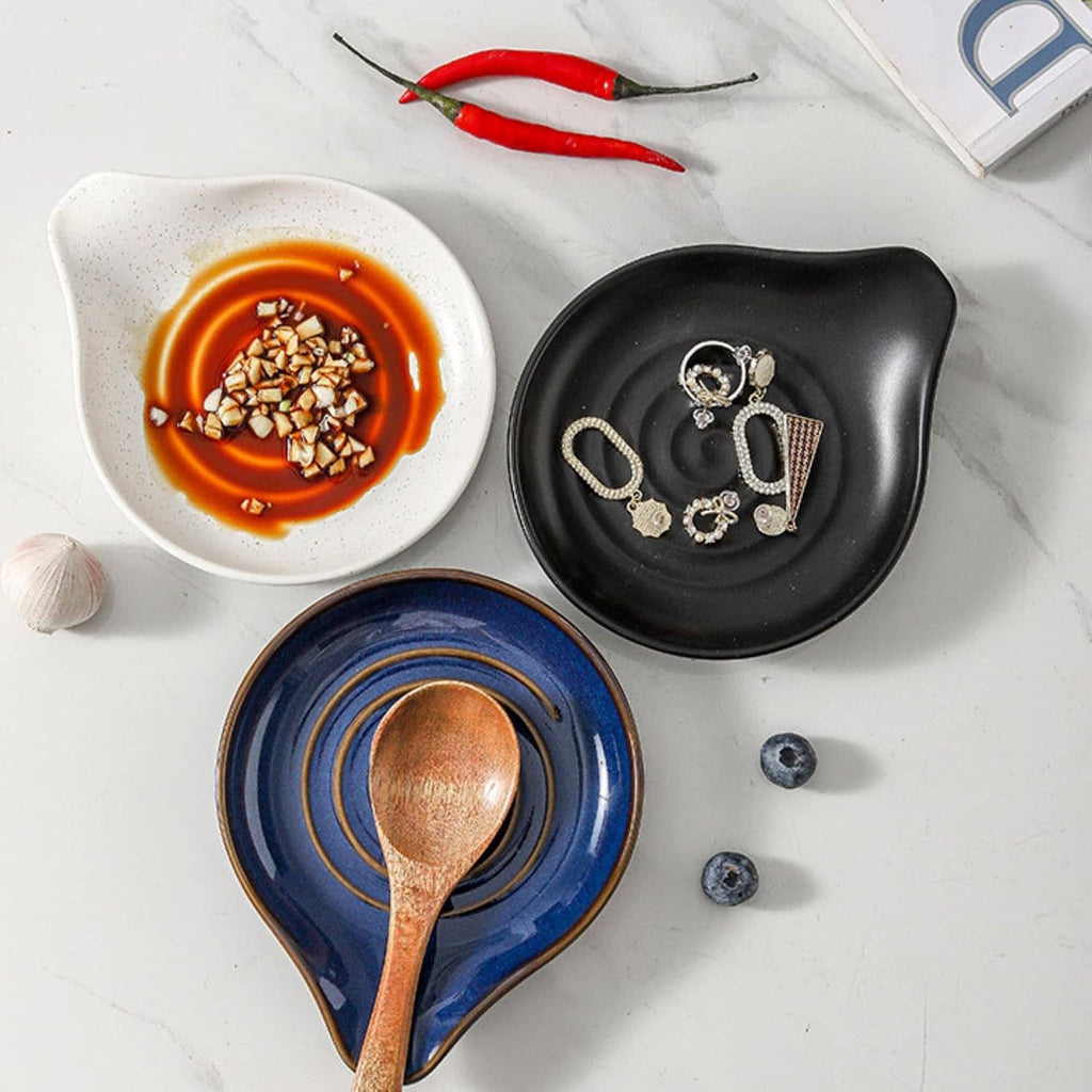 Black ceramic spoon rest with swirl pattern, with blue spoon rest beside it