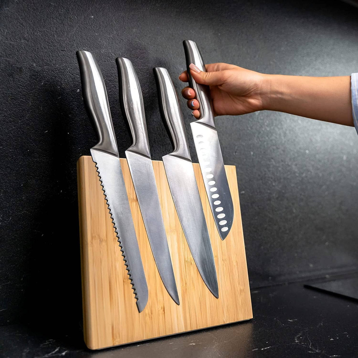 Coninx bamboo magnetic knife holder with knives; hand holding a chef knife