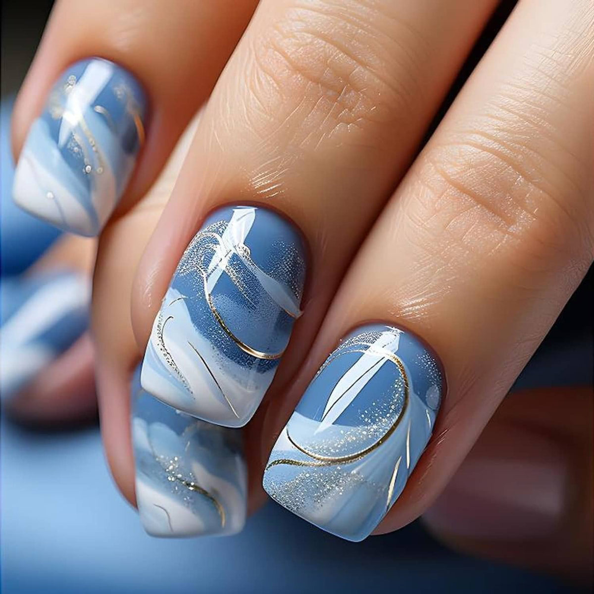 Close-up of blue square press-on nails with white swirls, glitter specks, and gold lines