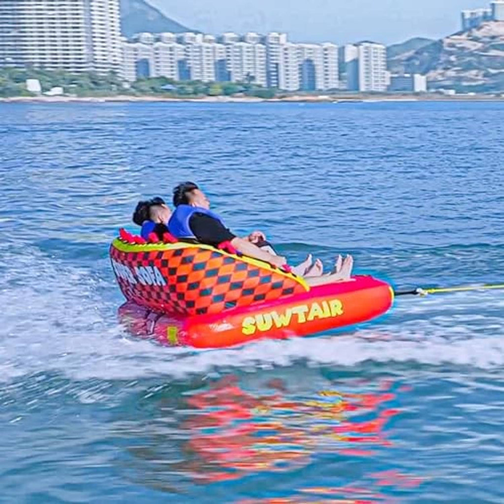 Inflatable towable pull tube with orange body and checker trim, carrying riders on water.