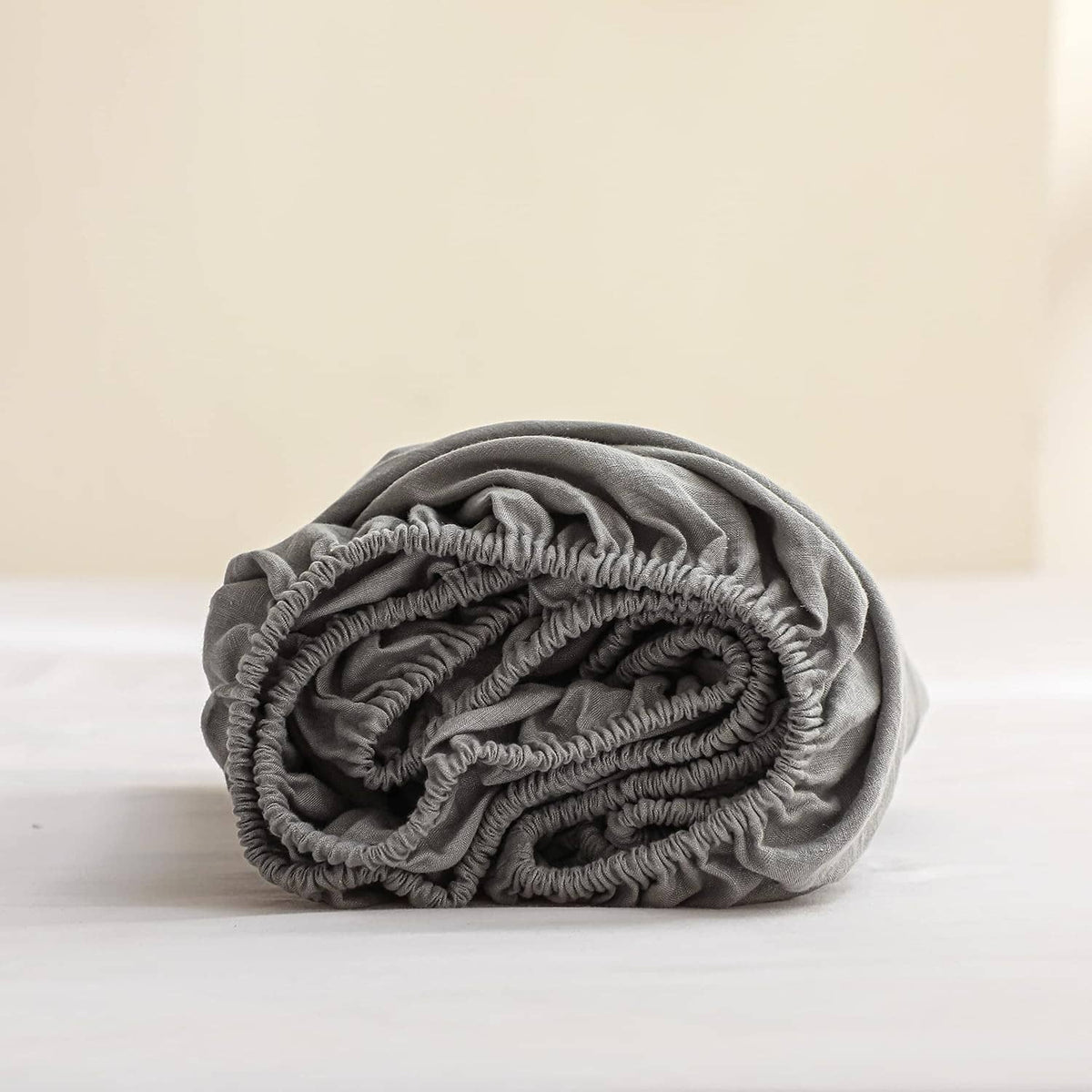 Gray linen fitted mattress cover rolled up with gathered elastic edge