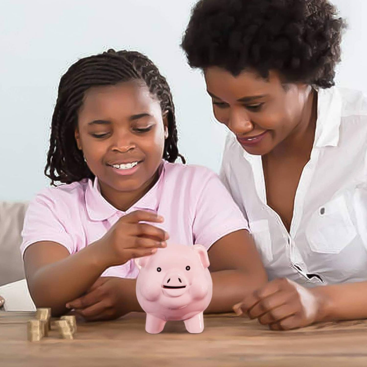 Pink ceramic piggy bank on a table, with kids nearby and smiling