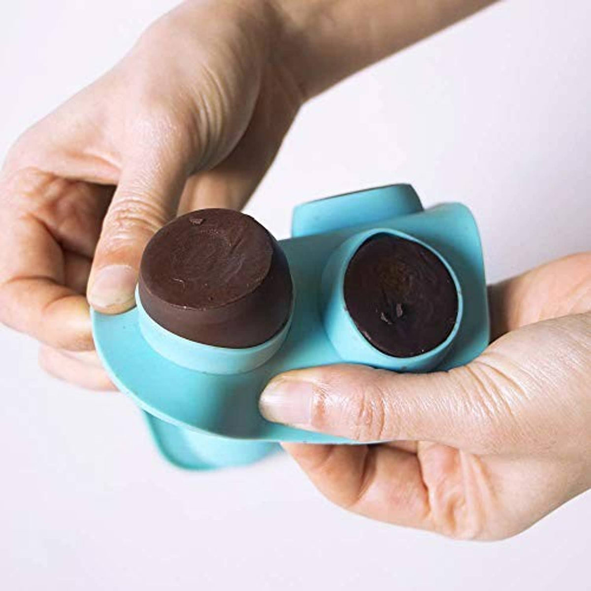 Silicone sphere chocolate mold held in hands, showing dark chocolate in one cavity