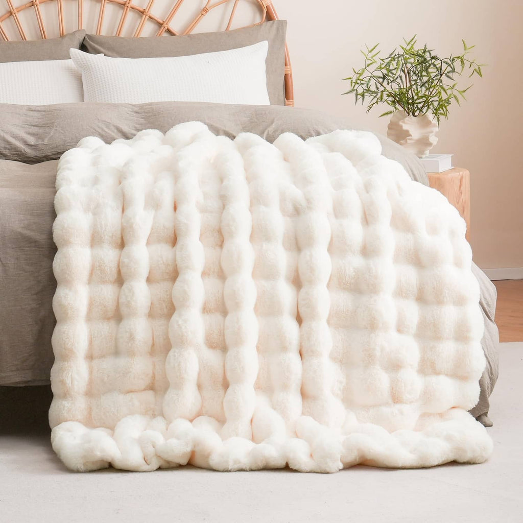 Cream faux fur throw blanket with bumpy bubble pattern, folded on a bed