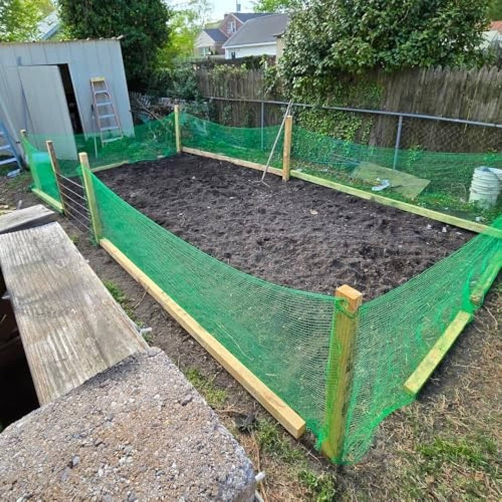 Green garden mesh fence enclosure around a raised garden bed with corner posts