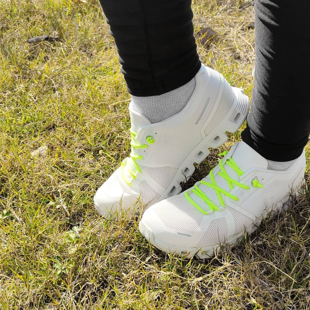 Elastic neon green shoe laces on white sneakers in grass