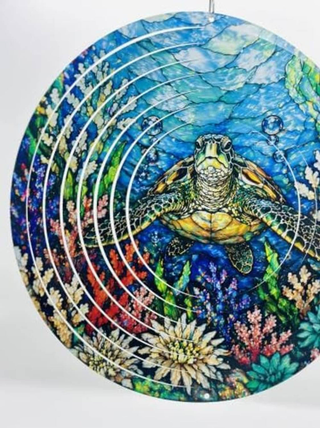 Close-up of round blue sea turtle wind spinner with metal ring swirls and ocean flowers.