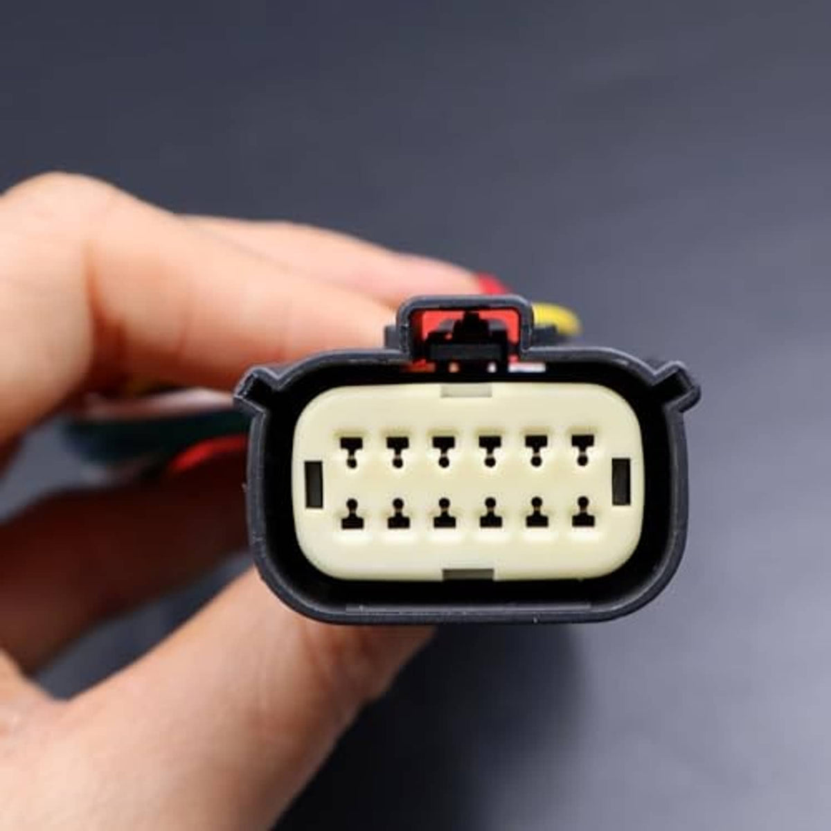 Multi-pin headlight connector plug held in hand, showing pin layout
