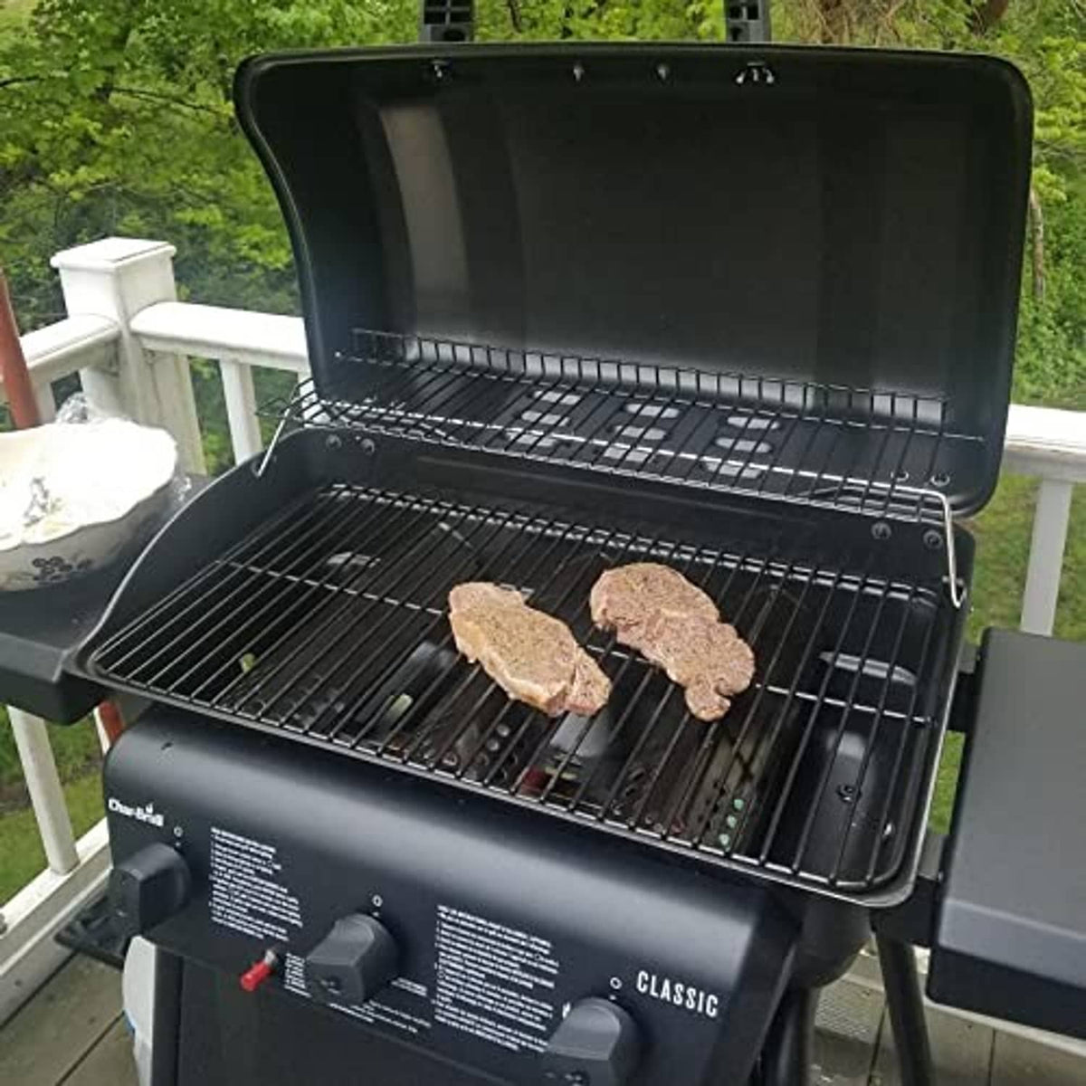 3-burner gas grill with black grates and two steaks cooking on the surface