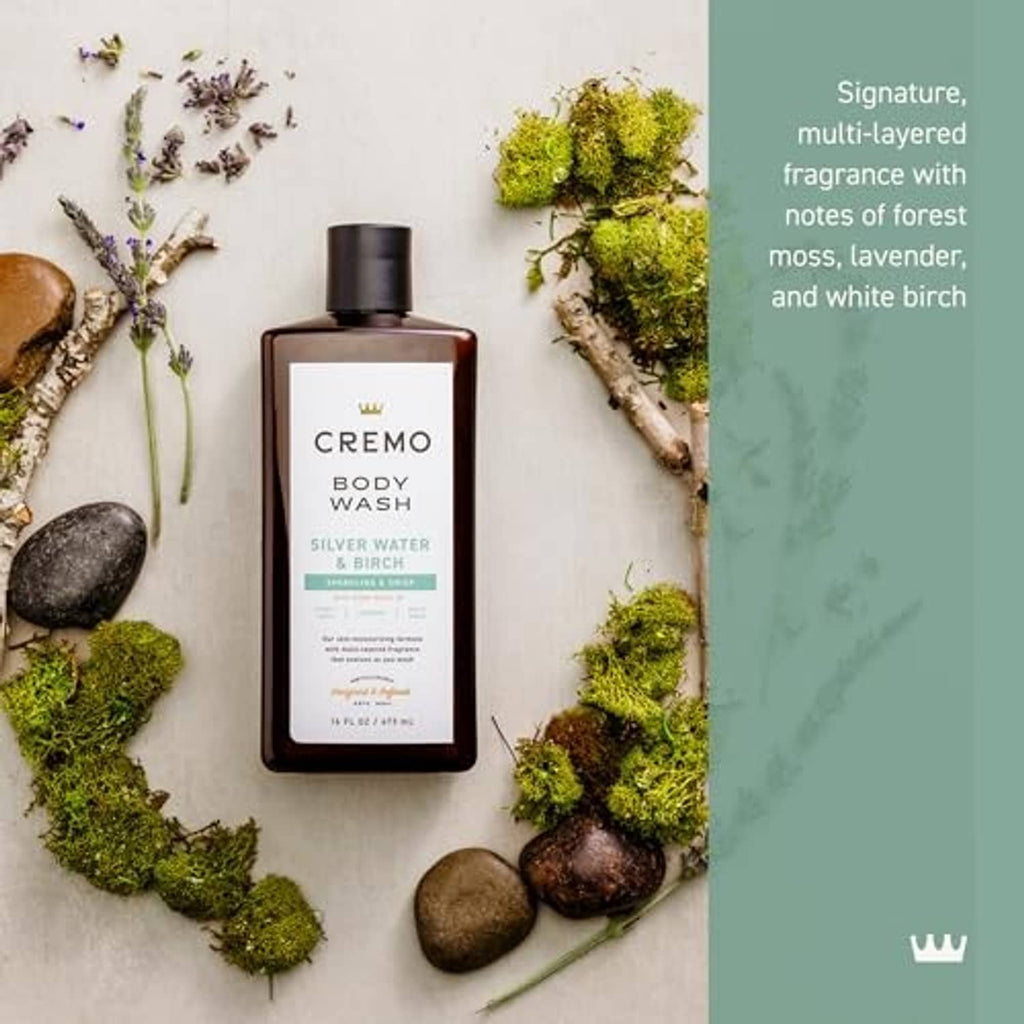 Cremo body wash bottle surrounded by moss, stones, and lavender sprigs, black cap