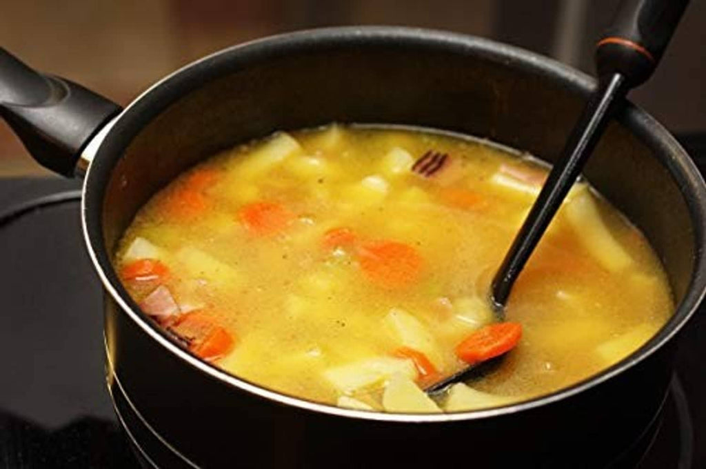 Pot of golden soup with carrots and greens, black ladle resting inside