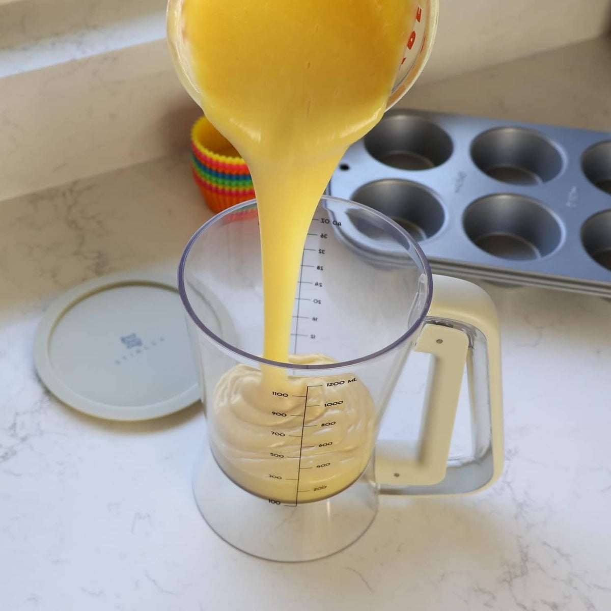 Beige batter dispenser pouring yellow batter into a small clear measuring cup