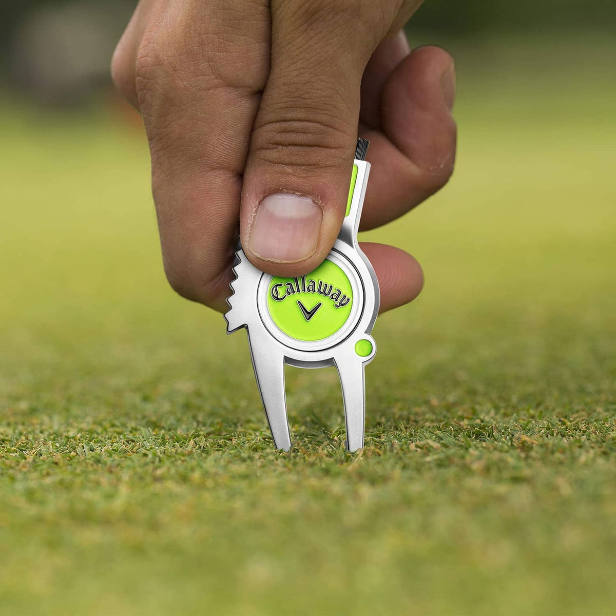 Hand holding a 4-in-1 golf divot repair tool with lime cap and Callaway logo
