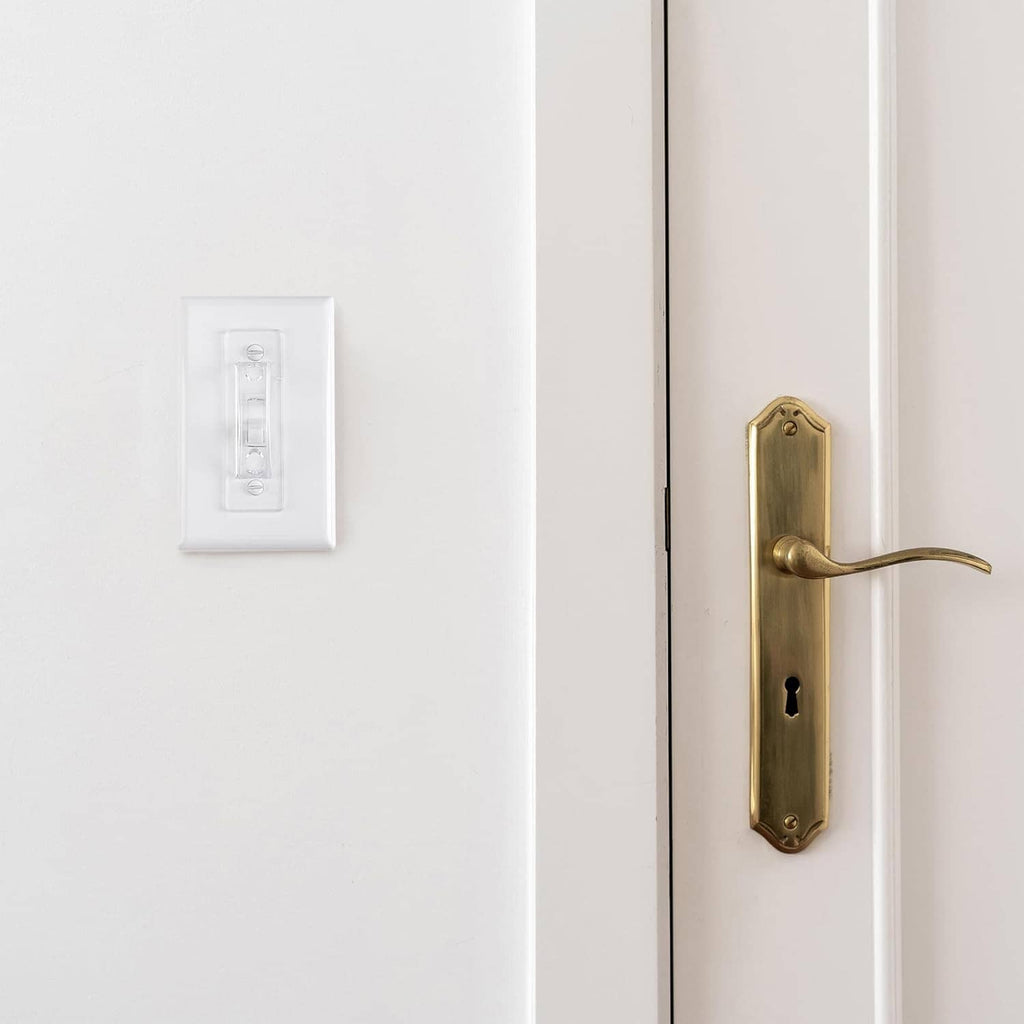 Clear toggle light switch guard cover installed on a white wall switch plate