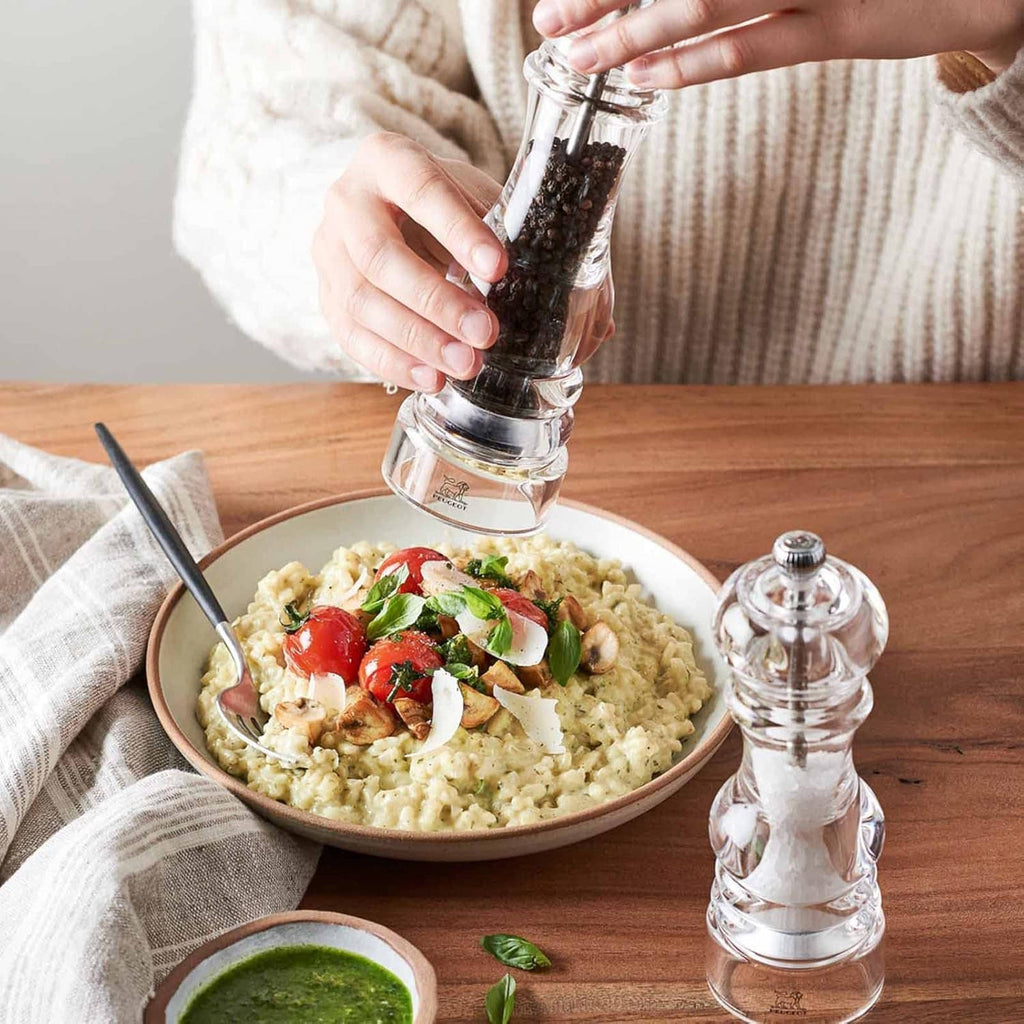 Pepper mill held above a bowl, with grinder top and clear body visible