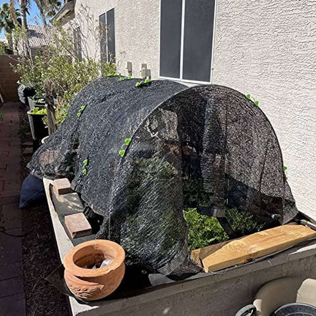 Black mesh-covered garden grow tunnel hoop frame on raised bed in outdoor yard