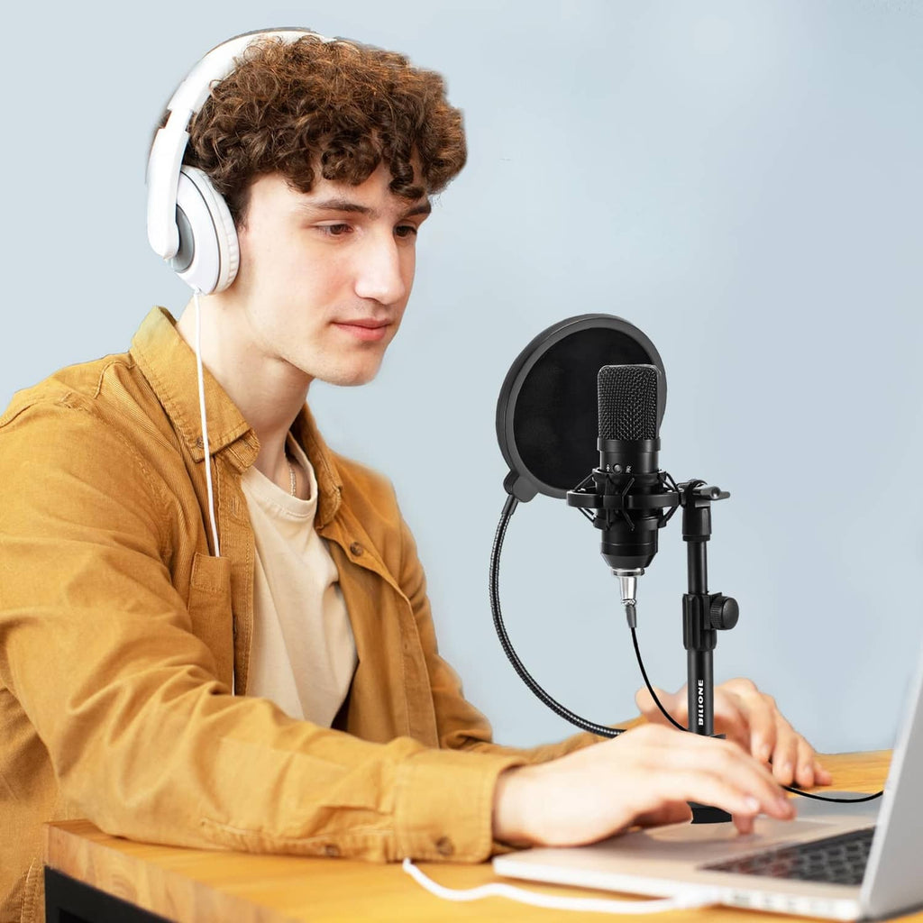 Black desktop microphone with shock mount on adjustable stand beside headphones