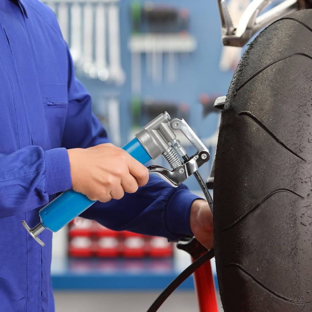 Blue grease gun held beside tire with chrome pump head and nozzle