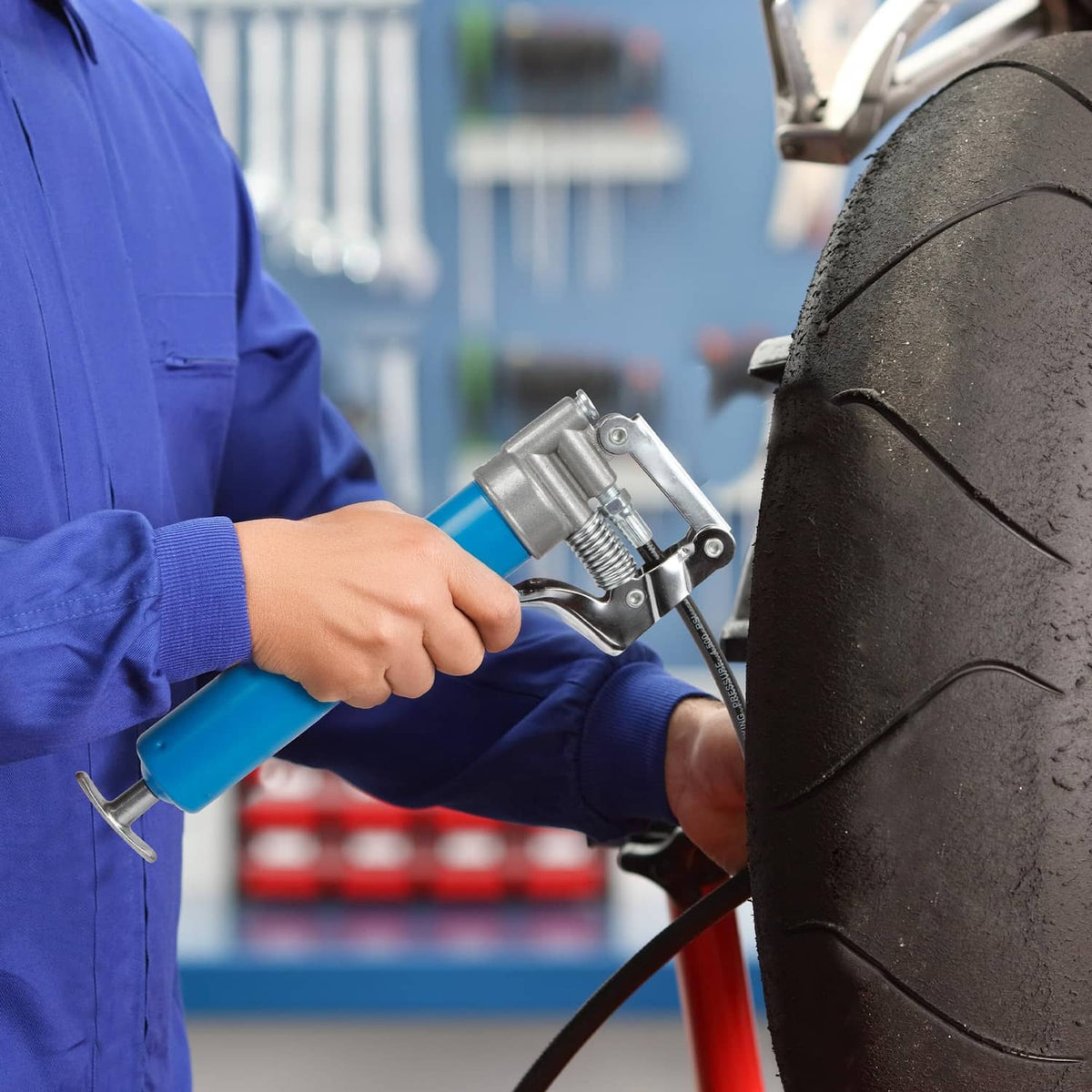 Blue grease gun held beside tire with chrome pump head and nozzle