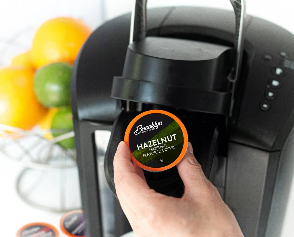 Hand placing a hazelnut flavored coffee pod into a black pod coffee machine