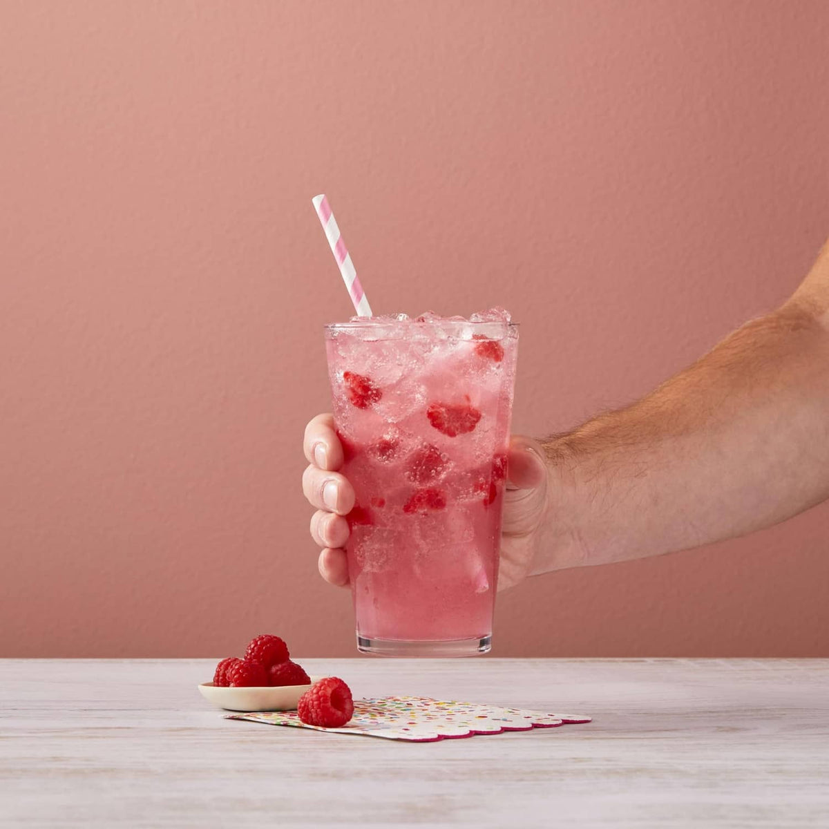 Hand holding a glass of raspberry syrup drink with crushed ice and raspberries
