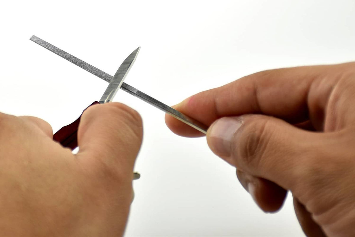 Diamond needle file being used by hands; silver tip and red handle visible