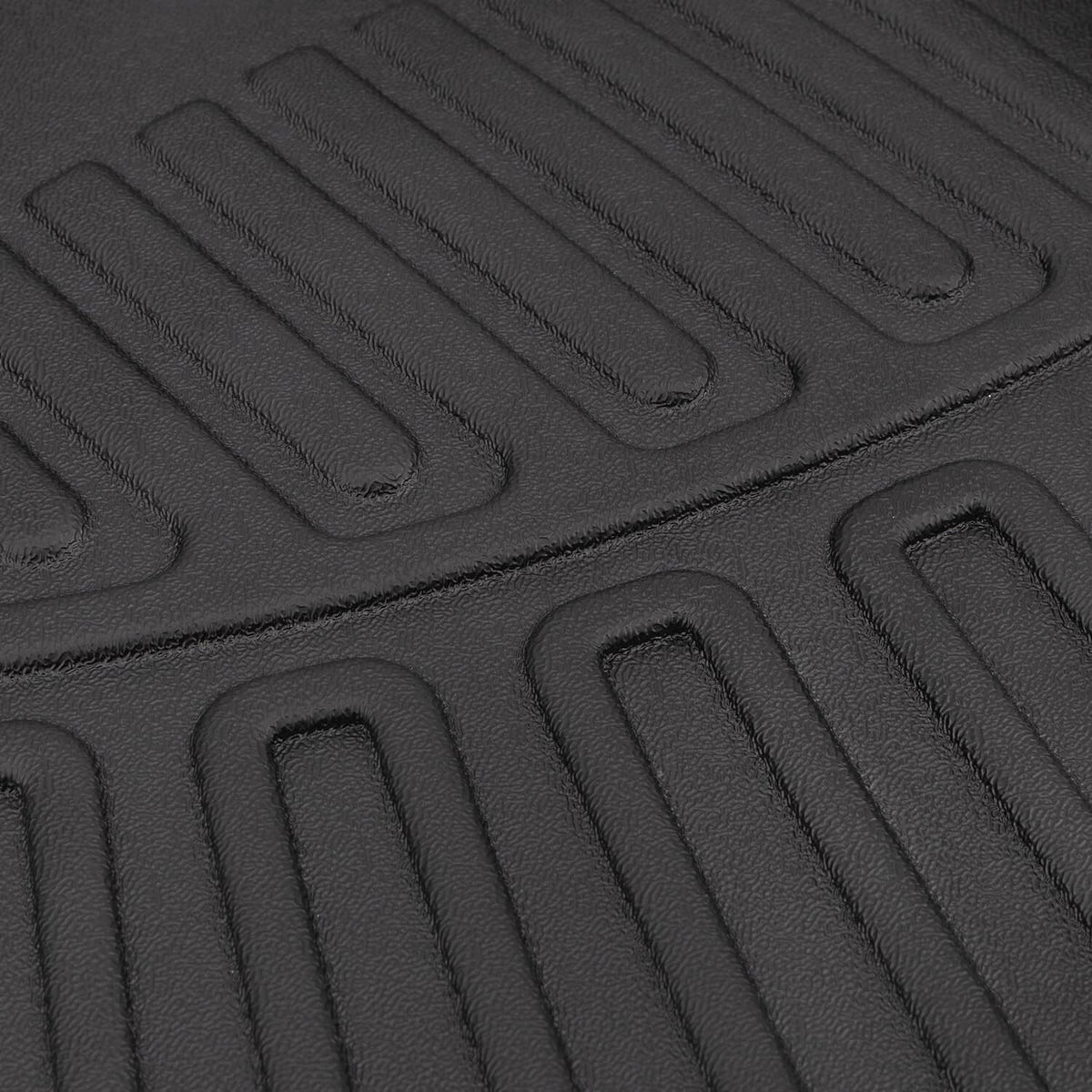 Textured close-up of black floor mat surface with raised lines and shallow channels