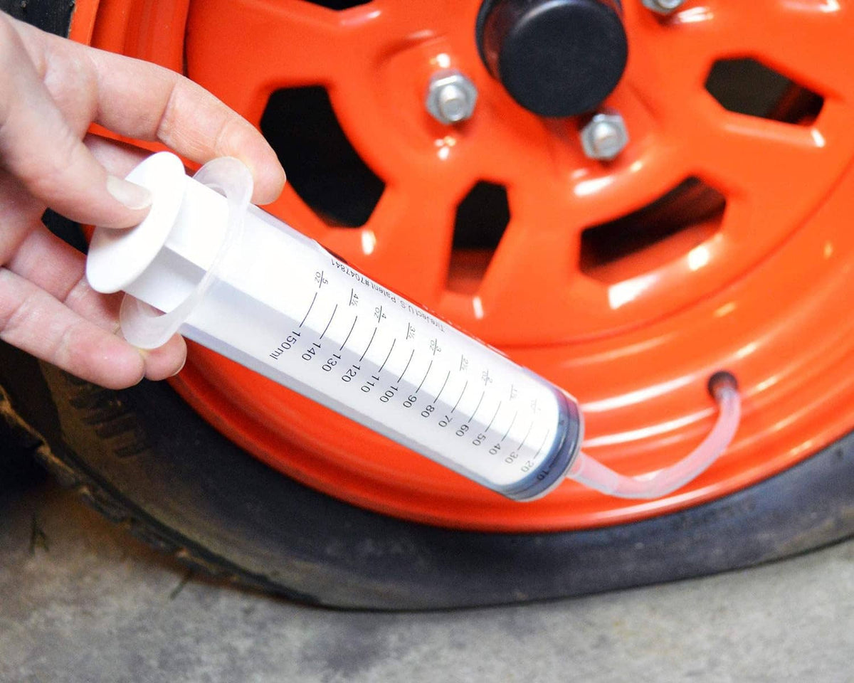 Tire sealant injector dispensing into a tire valve on an orange mower rim