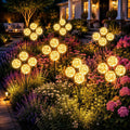 Warm white solar globe lights on black stakes, glowing among outdoor flowers