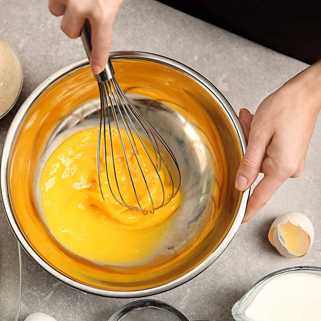 Stainless steel whisk mixing yellow batter in a round metal bowl