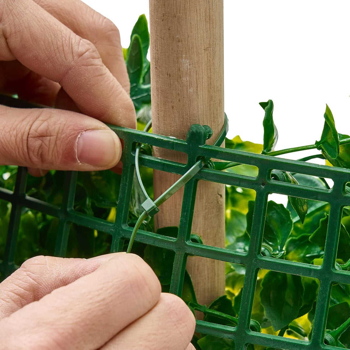 Green artificial plant wall panel with plastic grid and clips on a wooden pole