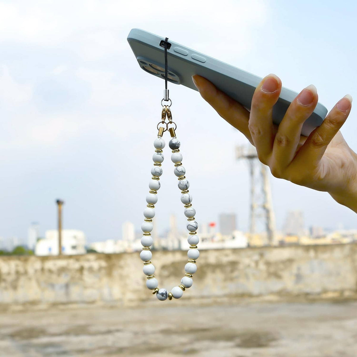 Marble white beaded phone wrist strap hanging from a handheld smartphone