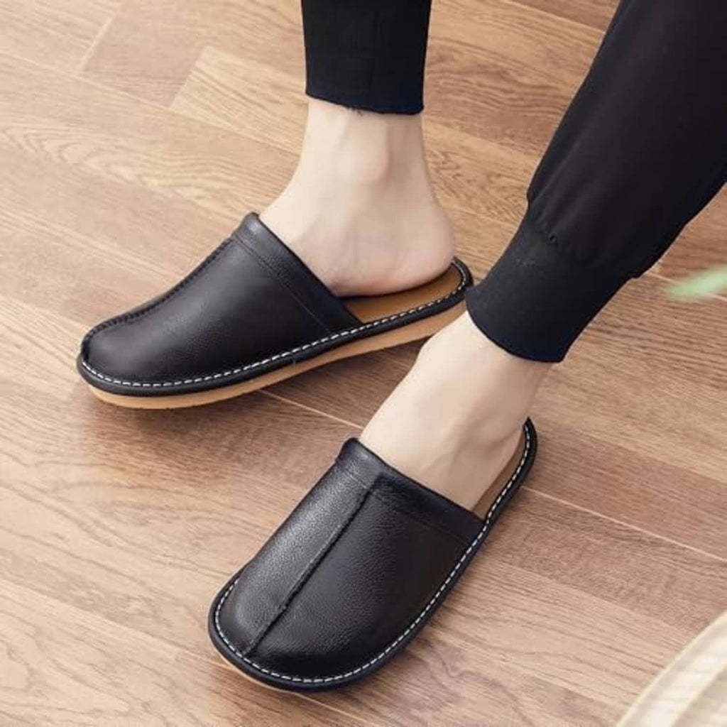 Black leather slippers worn with dark pants on a light wood floor