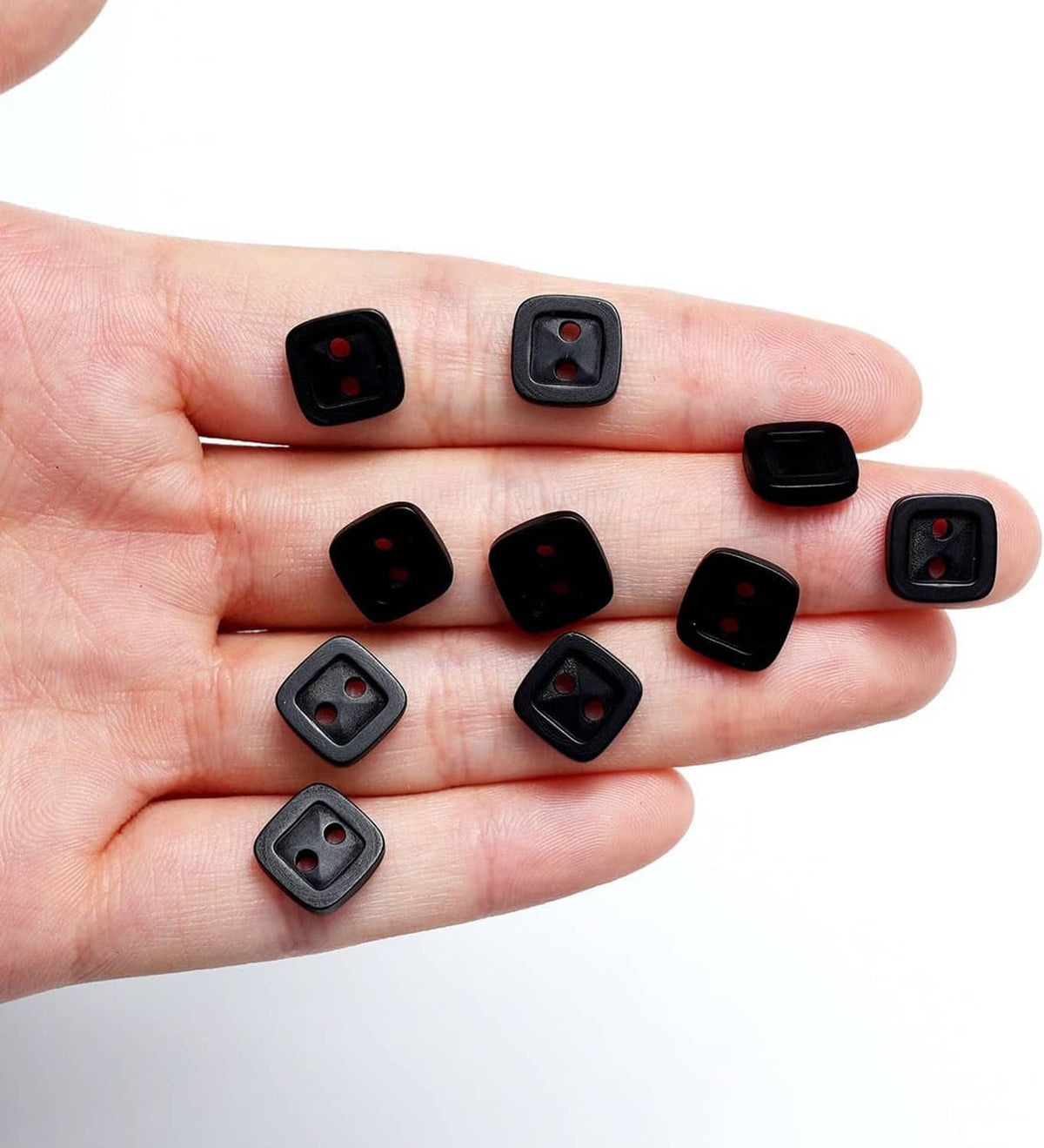 Black square 2-hole resin buttons on an open palm, mixed front finishes